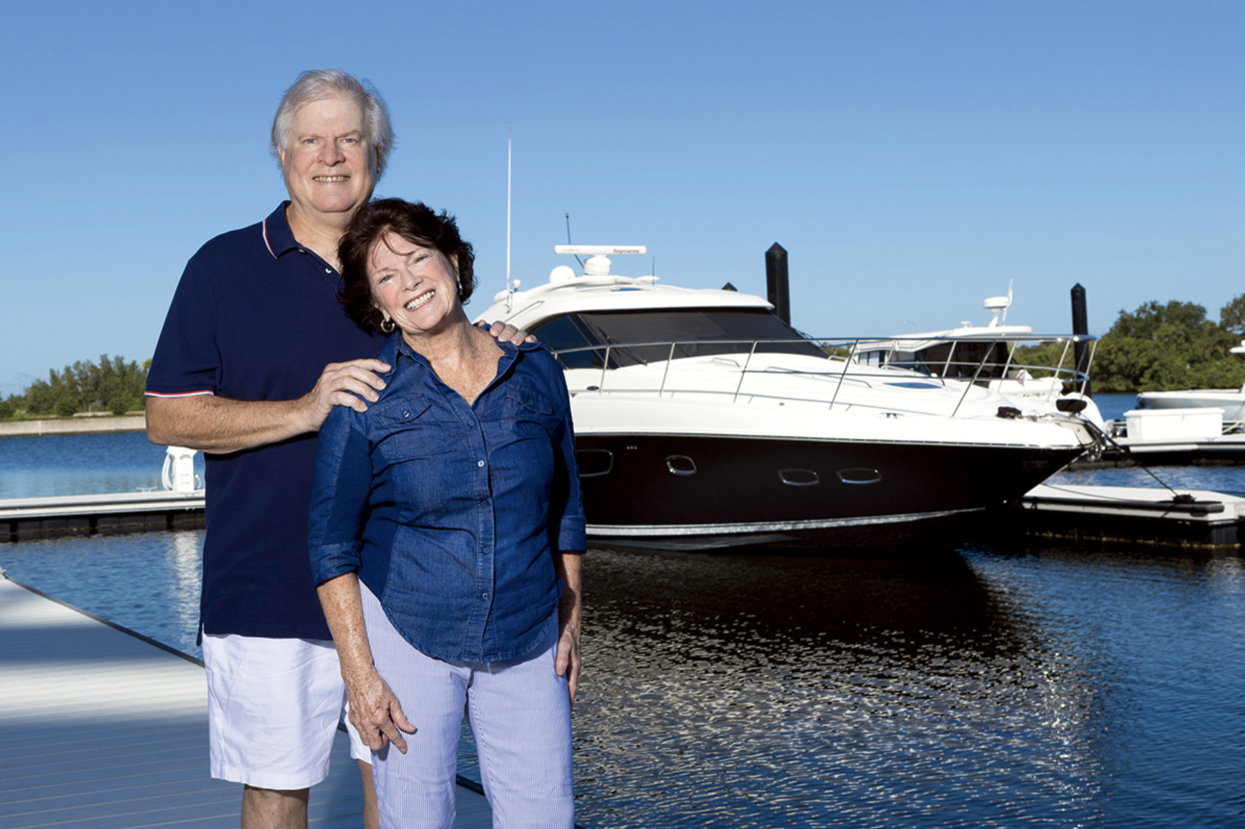 Mature couple smiling on a dock at Marina Pointe, Tampa, with a luxury yacht in the background, showcasing new construction waterfront condos with modern architecture, deepwater marina access, and resort-style amenities.